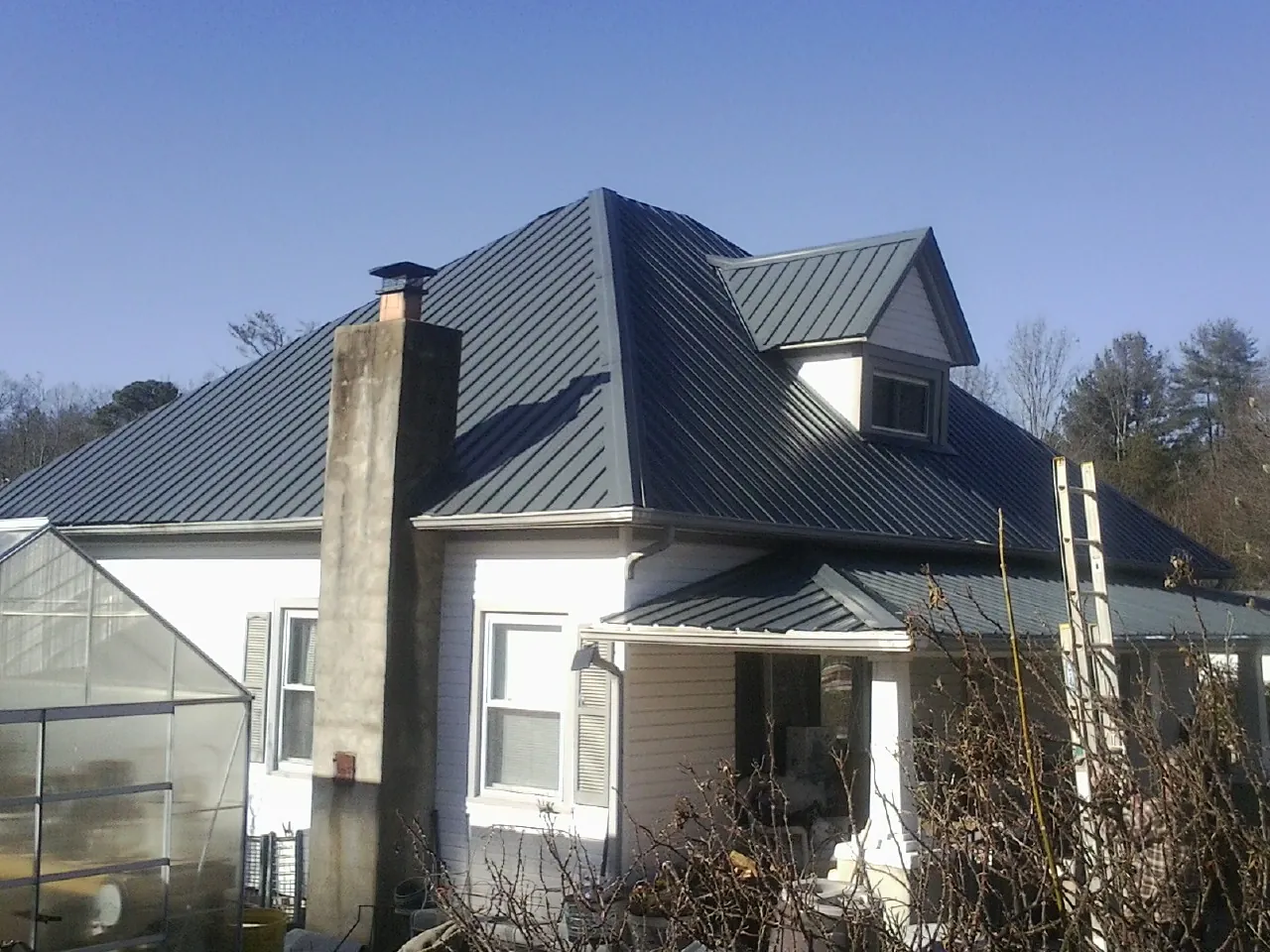 Dark blue standing seam metal roof on a white farmhouse with dormer — Slate & Tile Roof Repair by Roofing Brothers in Advent