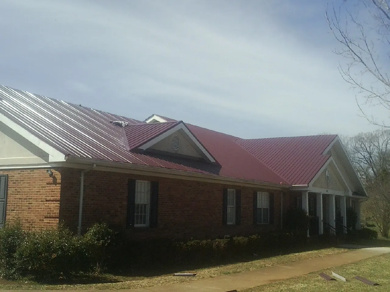 Red metal roof with gabled entries on a long brick building, from a Hail Damage Roof Repair job in Advent