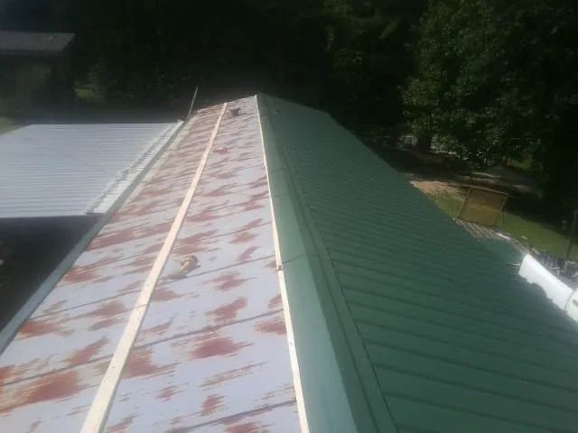 Old rusted panels beside newly installed green metal roofing — Wind Damage Roof Repair by Roofing Brothers in Advent