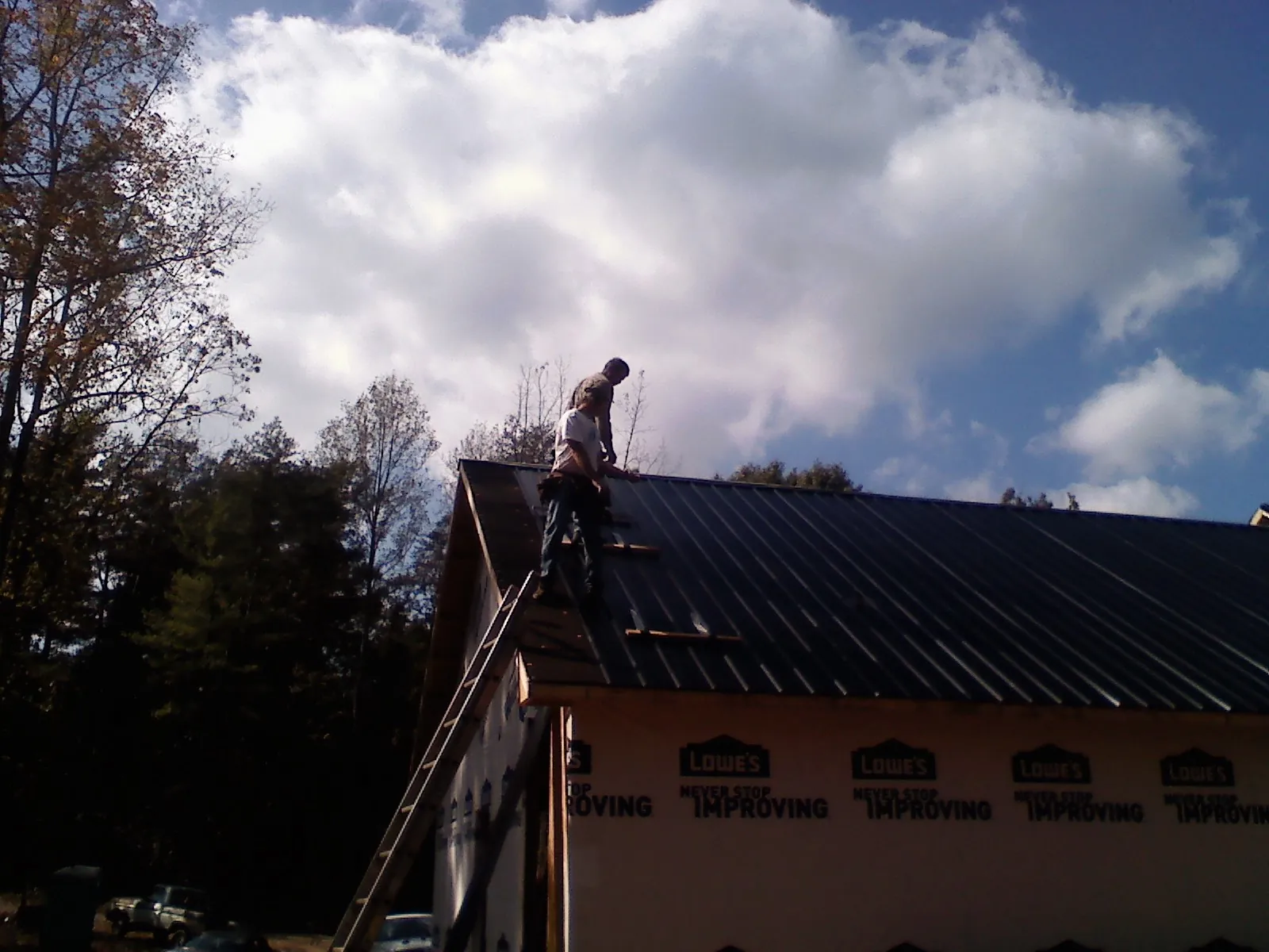 Roofer fastening dark metal panels high against a cloudy sky, from a Roof Inspection job in Advent